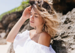 Pleasant girl posing near rock with eyes closed. Outdoor portrait of tanned sensual lady standing on nature background..